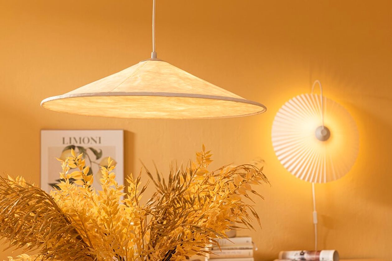 Hängelampe und Wandlampe vor gelber Wand, mit gelbem Laub und einem Bild im Hintergrund.