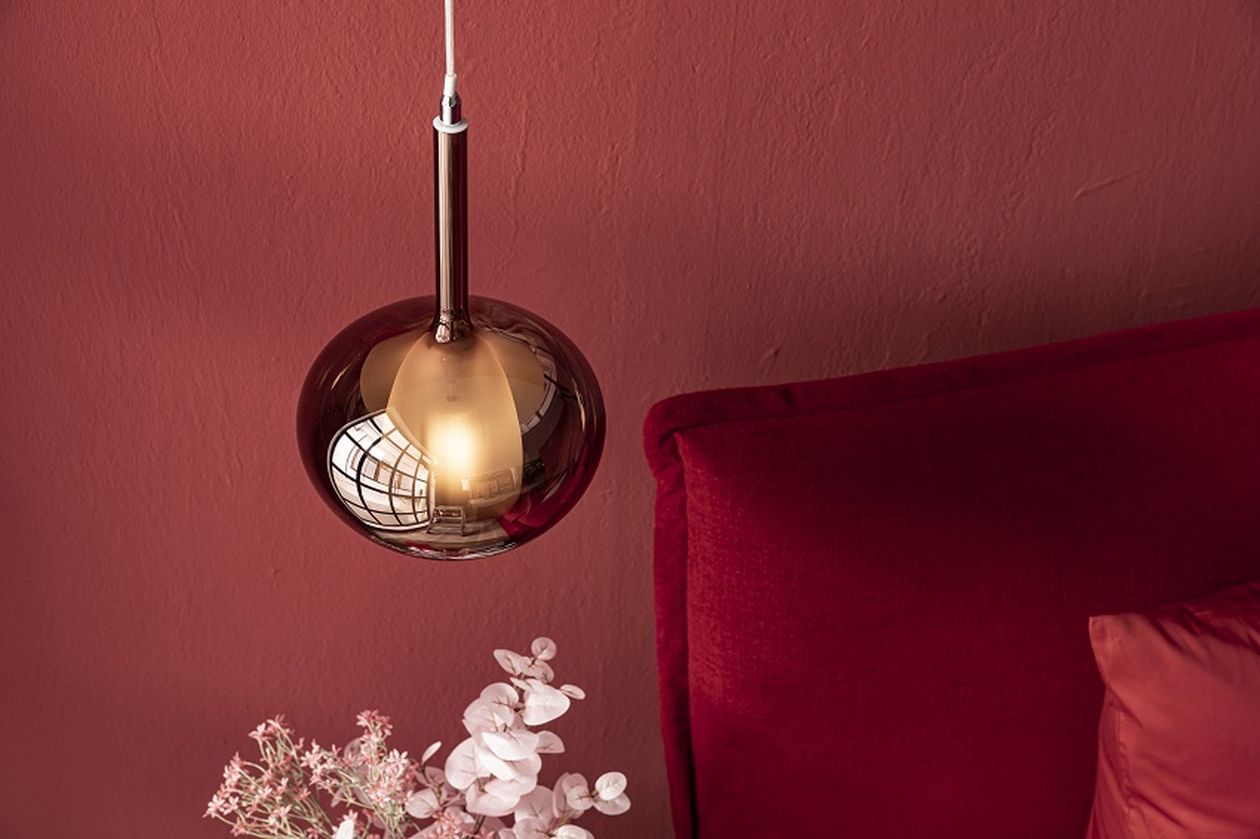 Rote Kugel-Lampe hängt über rotem Sofa mit Blumenstrauß im Vordergrund, vor einer roten Wand.