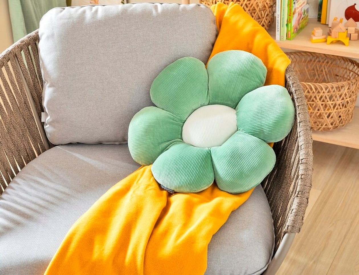 Gemütlicher Lesesessel in einem freundlich gestalteten Babyzimmer mit gelber Kuscheldecke und grünem Kissen in Blumenform.