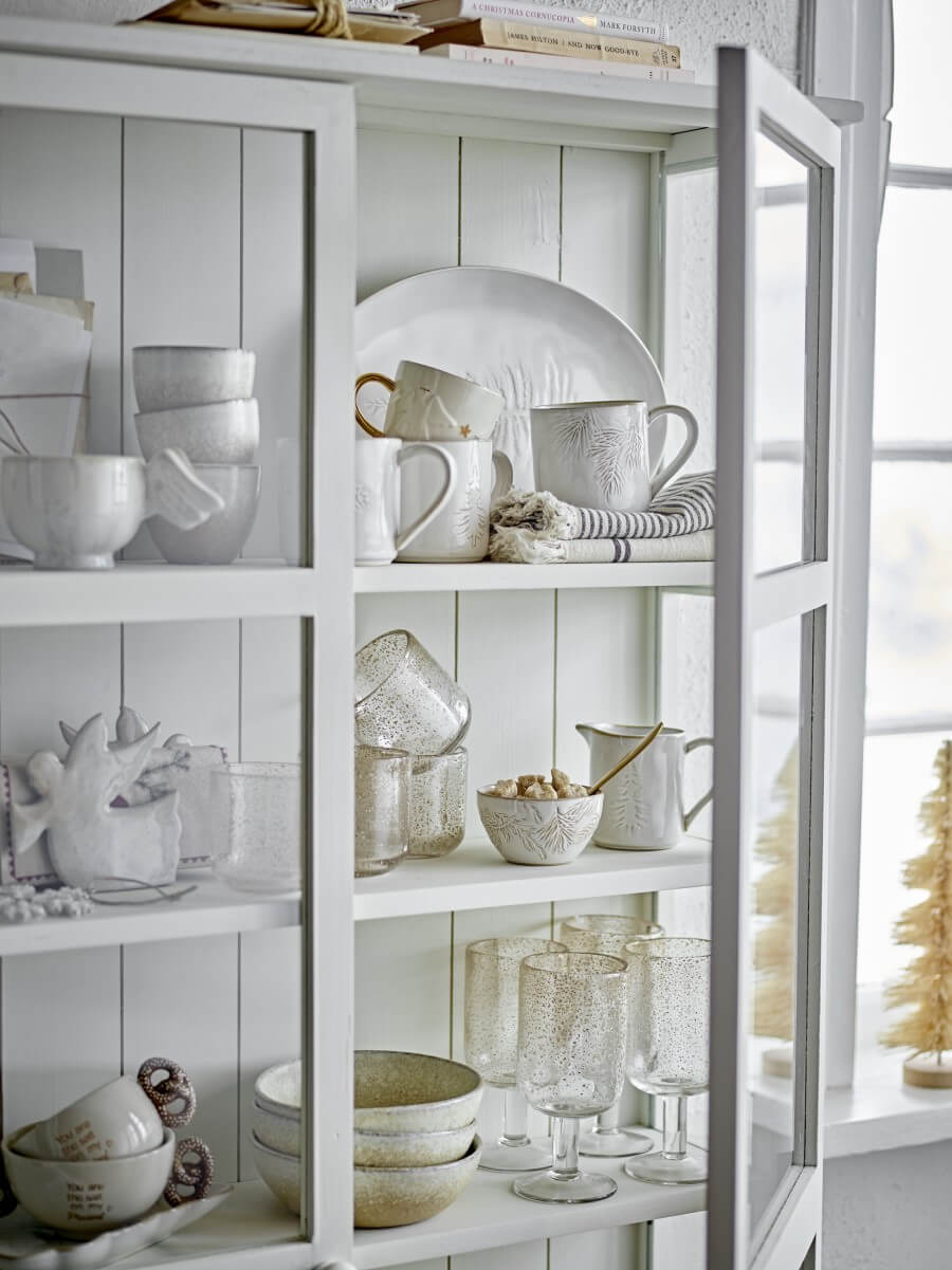 Weiße, geräumige Vitrine mit weißem Essgeschirr wie Gläser, Schüsseln und Tellern. Beide Türen sind verglast, im Hintergrund kommt Tageslicht durch großes Fenster.