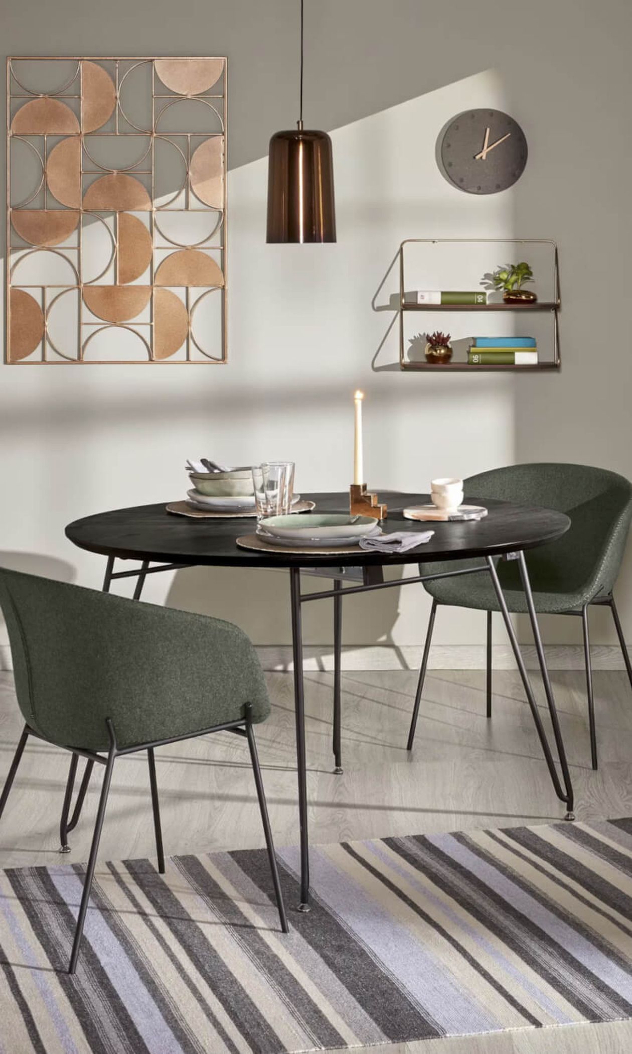 Essbereich mit einem ovalen schwarzen Tisch, grauen Stühlen, einem gestreiften Teppich, einer Kerze und dekorativen Wandelementen vor einem neutralen Hintergrund.