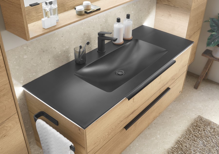 Modernes Badezimmer mit einer eleganten schwarzen Arbeitsplatte und einem Waschbecken, Holzschränken, einem schwarzen Wasserhahn, Pflegeprodukten und einem Handtuch auf einem Ständer.