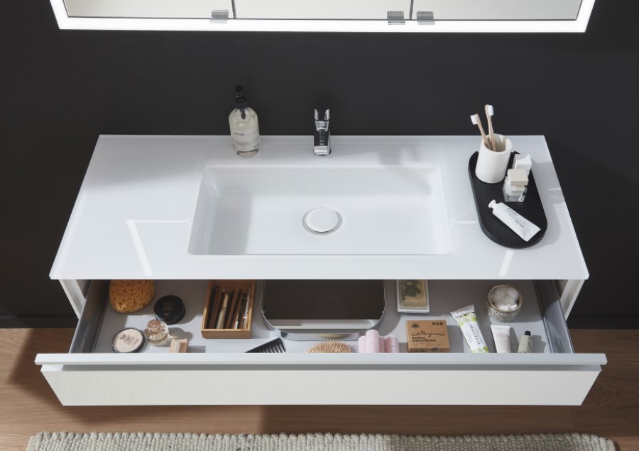 Moderner Badezimmerwaschtisch mit weißem Waschbecken, Wasserhahn und offener Schublade mit Pflegeartikeln. Schwarze Wand und Spiegel oben.