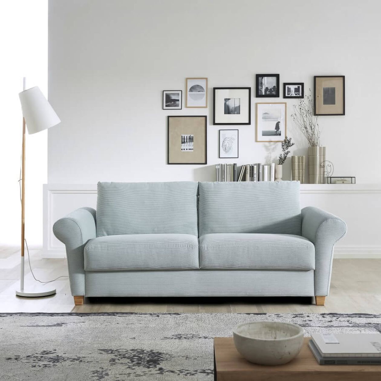 Hellblaues Sofa in einem minimalistischen Wohnzimmer mit einer Stehlampe und gerahmten Bildern an einer weißen Wand.