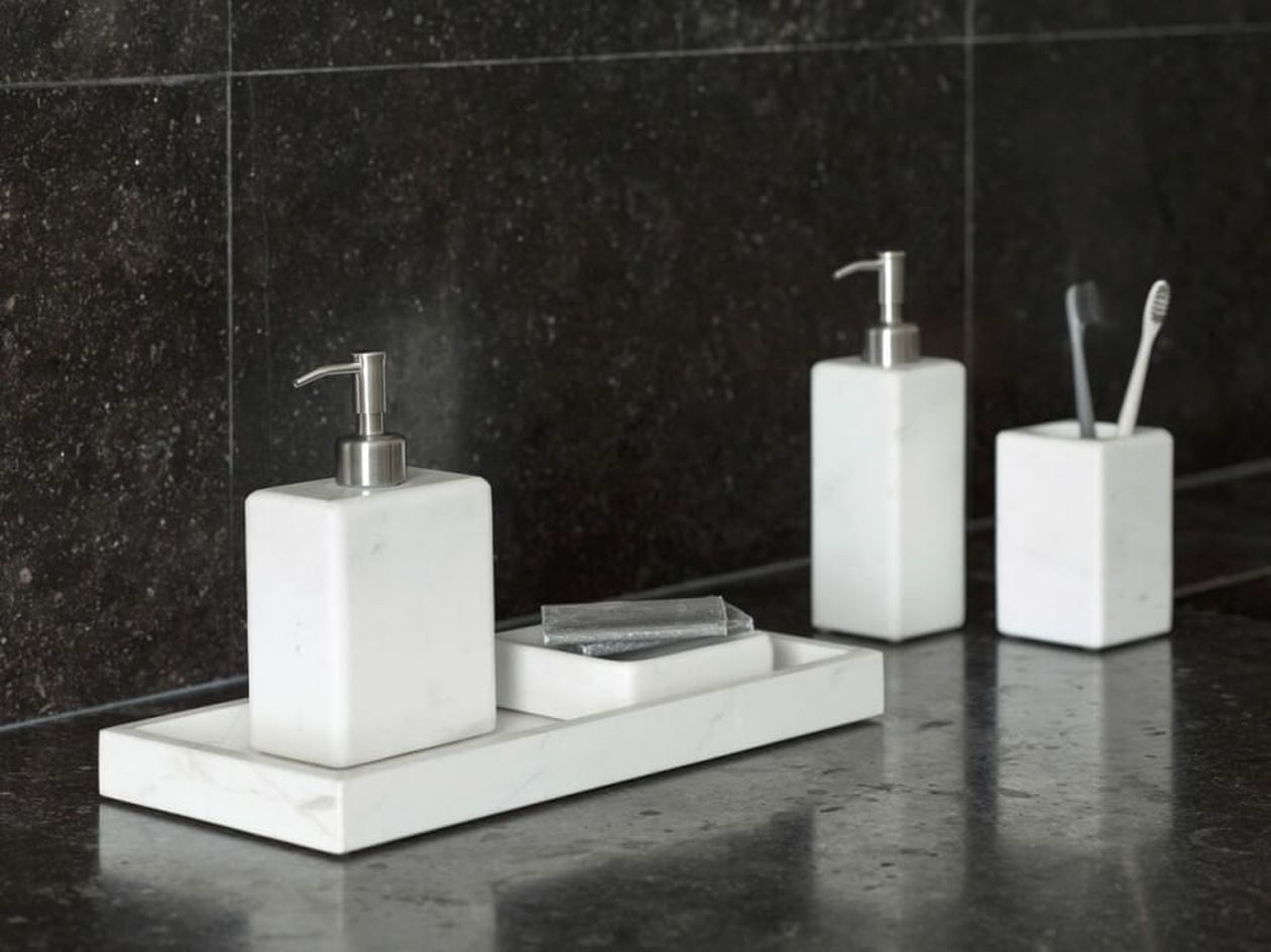 Marmor-Badezimmer-Set mit Seifenspendern, einer Seifenschale und einem Zahnputzbecher auf einer dunklen Granitplatte.