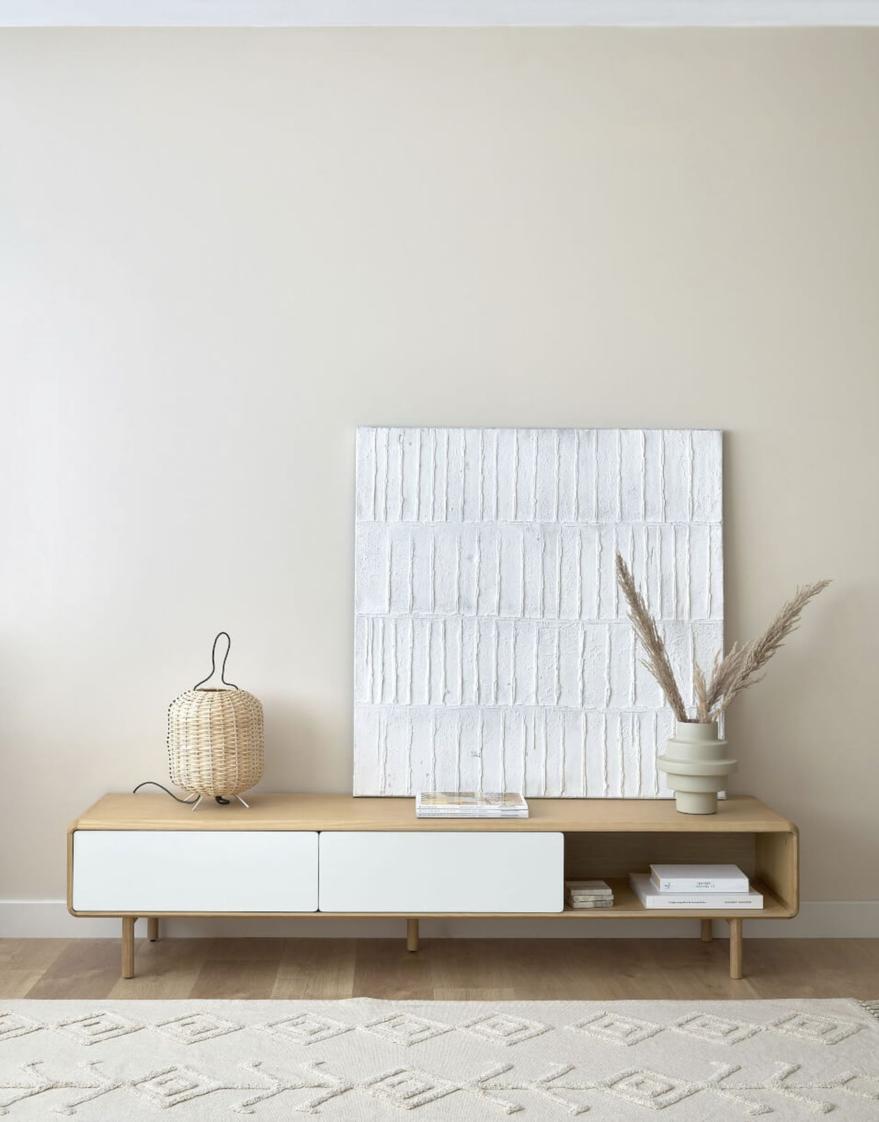 Minimalistisches Wohnzimmer mit einem Konsolentisch aus Holz, weißer Leinwand, Korblampe und Vase mit Pampasgras vor einer beigen Wand.