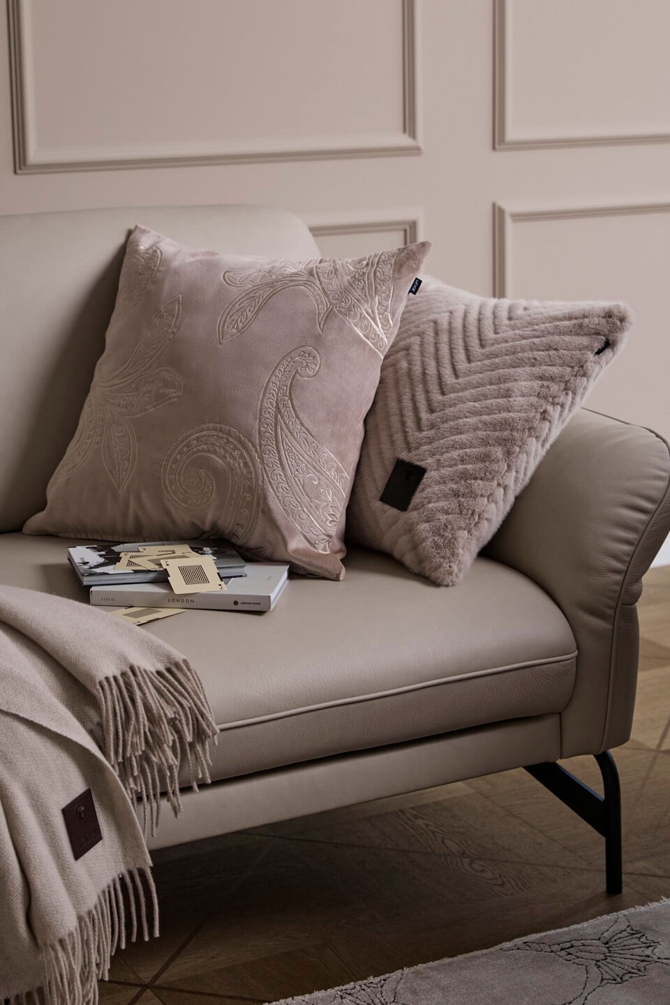 Ein beiges Sofa mit zwei Zierkissen, eines mit Paisleymuster und das andere mit Strukturdesign, und einer Überwurfdecke mit Fransen.