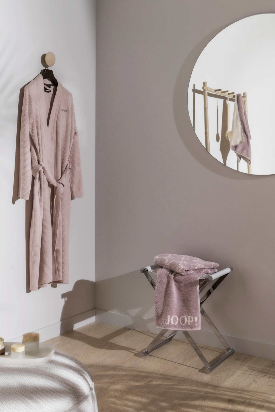 Helles Badezimmer mit einem Hocker und darauf die JOOP!-Duschtücher Doubleface und Cornflower in Rosa und dem Bademantel Kimono an der Wand an einem Haken