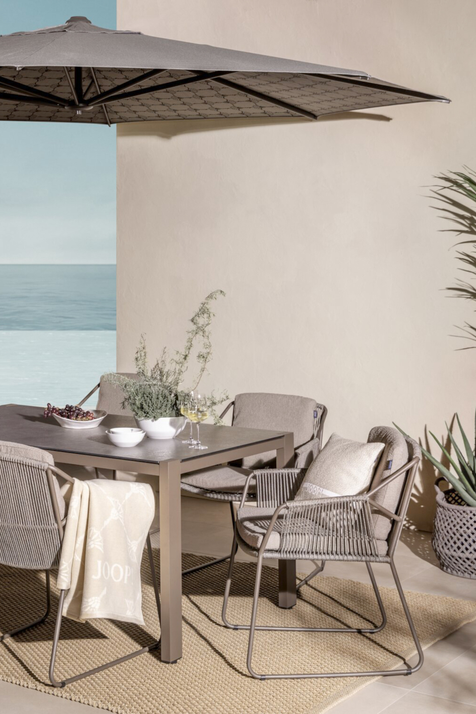 JOOP! Gartensessel Sharp in Beige aus Edelstahl und Rope auf einer mediterranen Terrasse mit Esstisch mit Blick aufs Meer