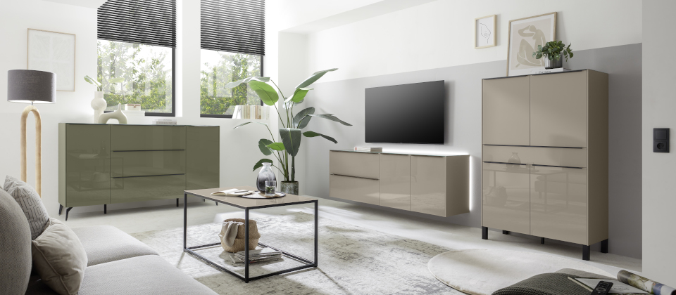 Modernes Wohnzimmer mit eleganten Möbeln, einem an der Wand montierten Fernseher, großen Fenstern mit Jalousien und Topfpflanzen auf hellem Boden.