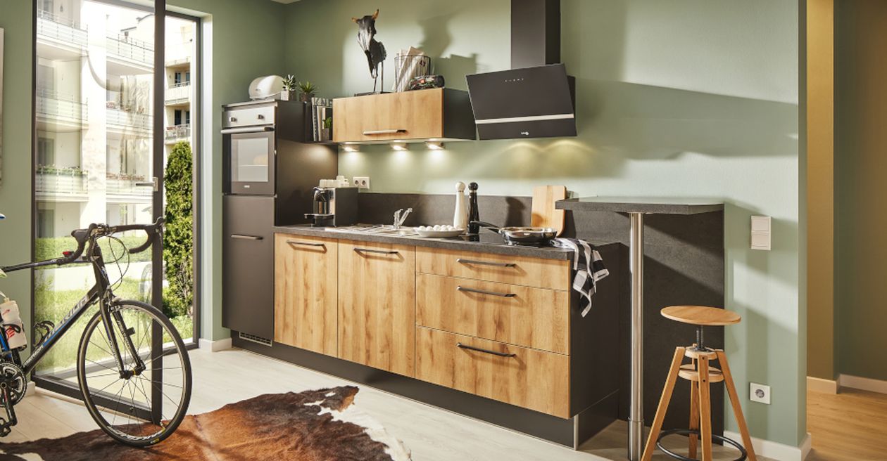 Moderne Küche mit Holzschränken, schwarzen Geräten und Dunstabzugshaube, grünen Wänden, Frühstücksbar mit Hocker, Fahrrad am hohen Fenster und Kuhfellteppich.