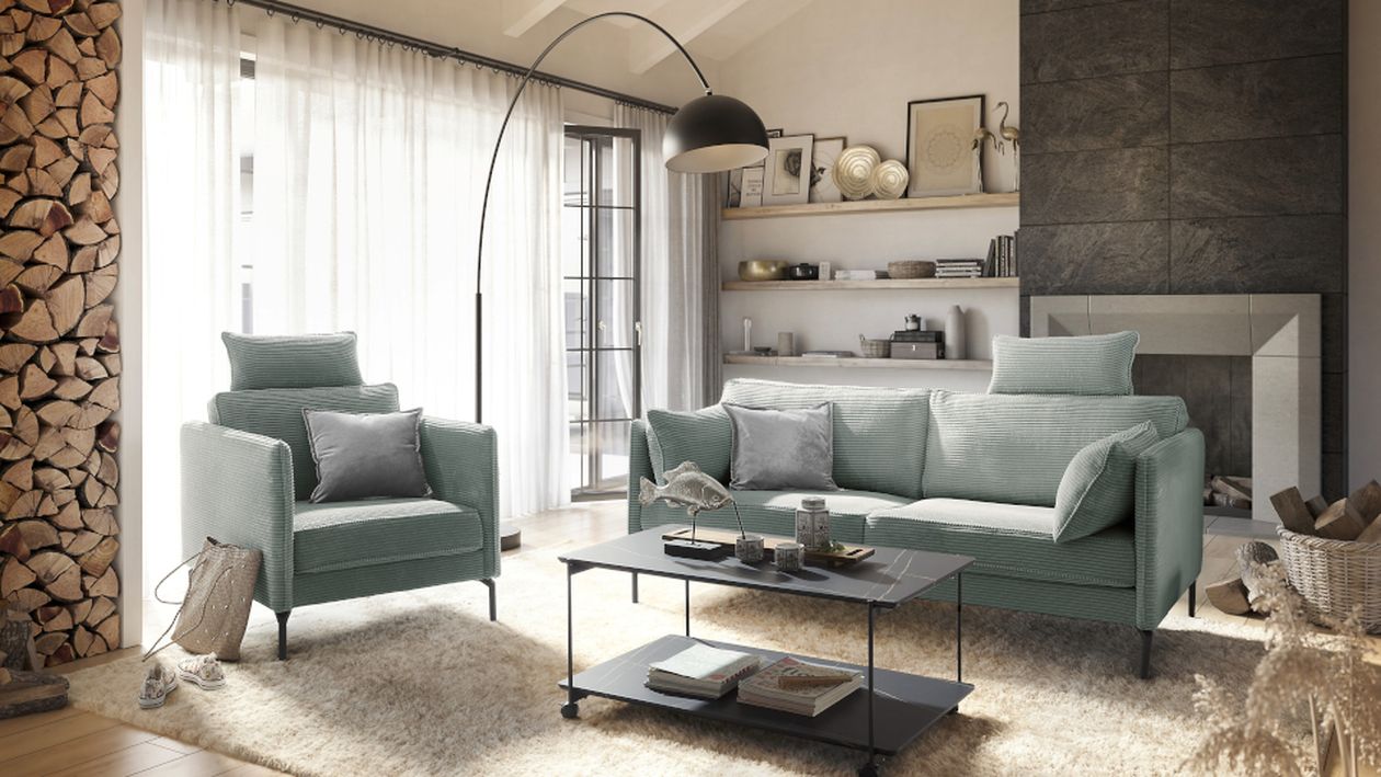 Wohnzimmer mit salbeigrünem Sofa, Sessel, Kamin und Regalen, einer Holzstack-Wand, Stehlampe und flauschigem Teppich.