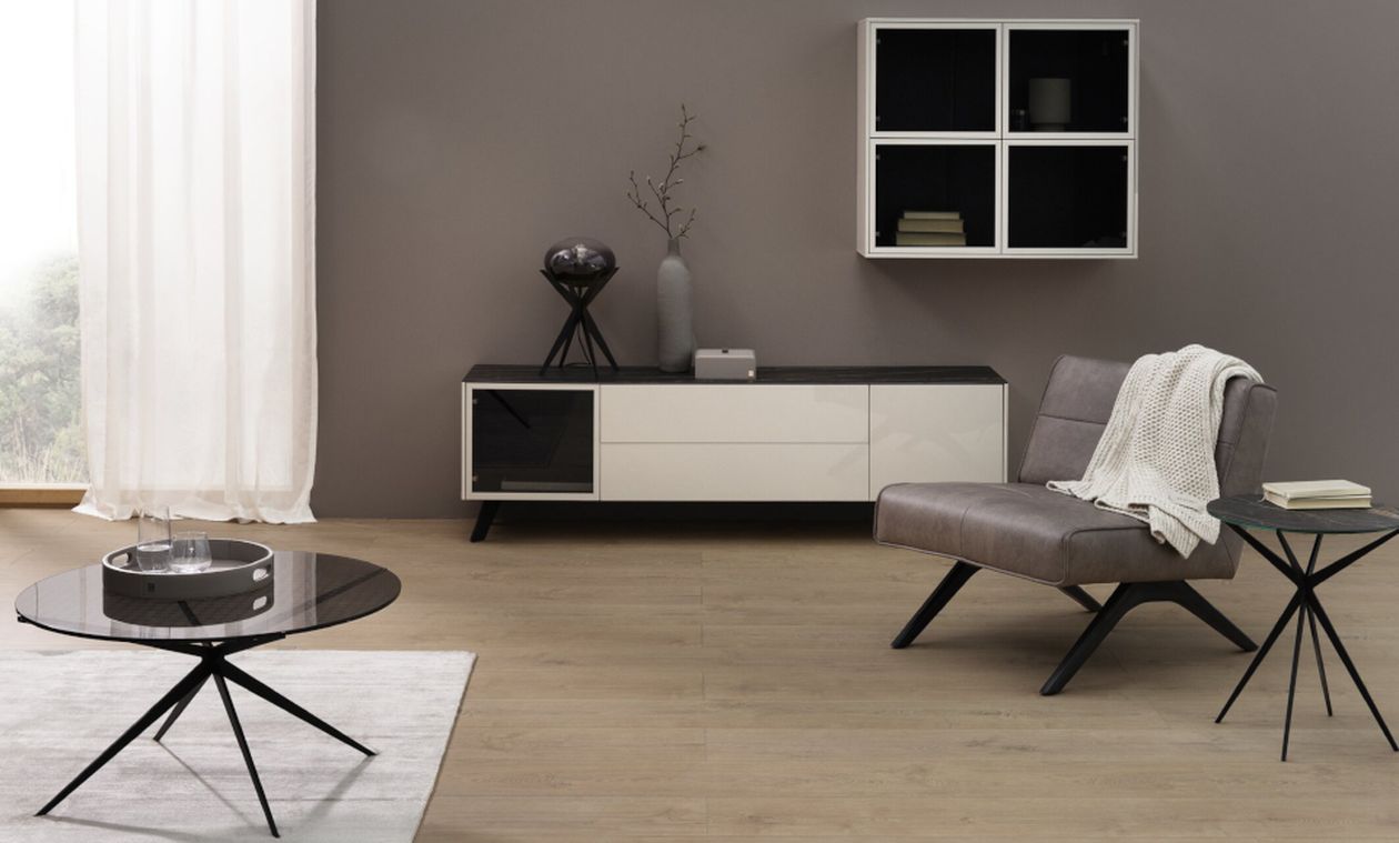 Modernes Wohnzimmer mit grauer Sitzgruppe, schwarzem Beistelltisch, Sideboard, Vase und einem Bücherregal an der Wand.