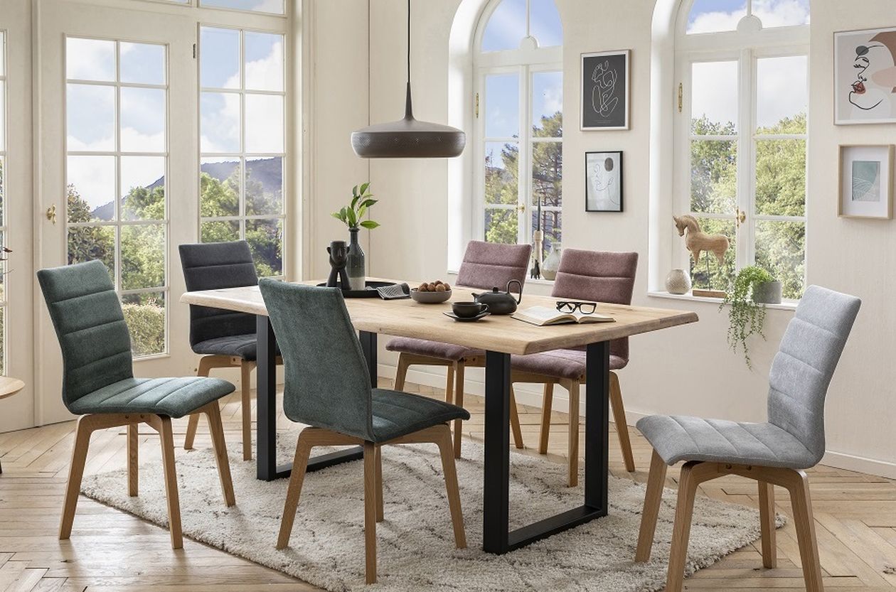 Modernes Esszimmer mit Holztisch, sechs farbenfrohen Stühlen, Pendelleuchte und großen Fenstern mit malerischem Ausblick.