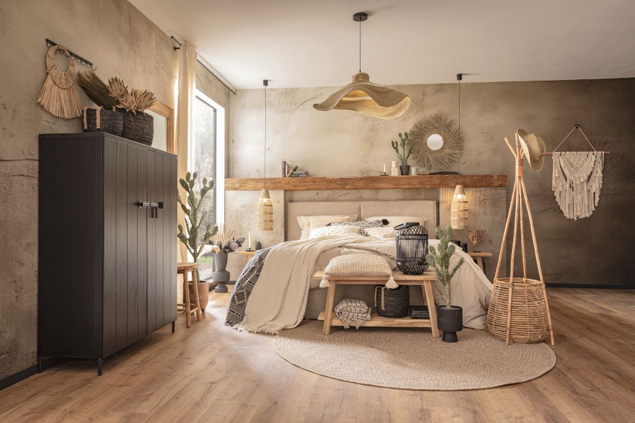 Gemütliches Schlafzimmer im Bohème-Stil mit Holzbett, neutraler Bettwäsche, gewebtem Teppich, Pendelleuchte, Pflanzen, Kleiderschrank und Makramee-Wanddekoration.