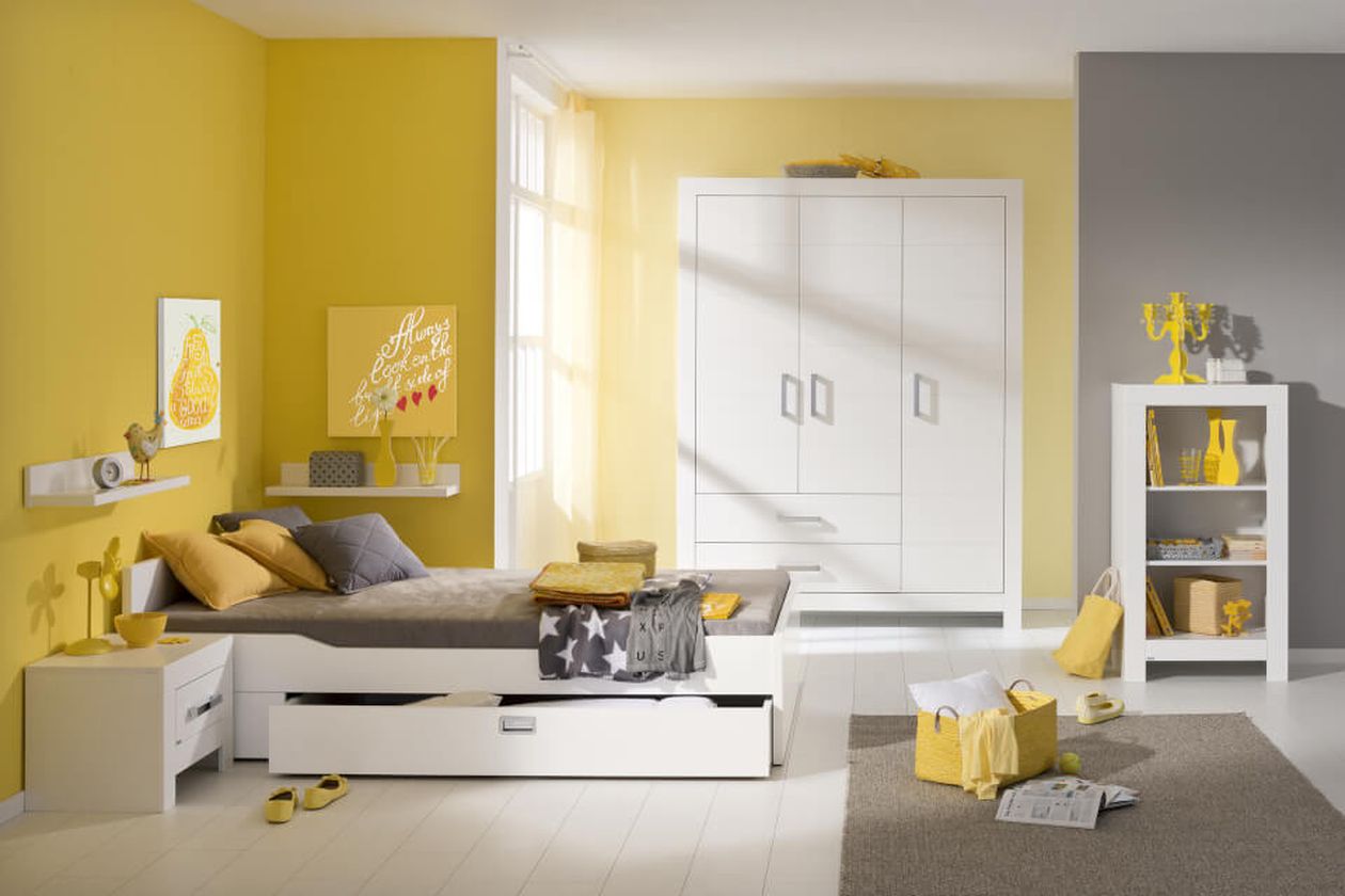 Ein modernes Schlafzimmer mit gelben und grauen Akzenten, ausgestattet mit Bett, Kleiderschrank, Regalen mit Dekoration und natürlichem Licht durch ein Fenster.