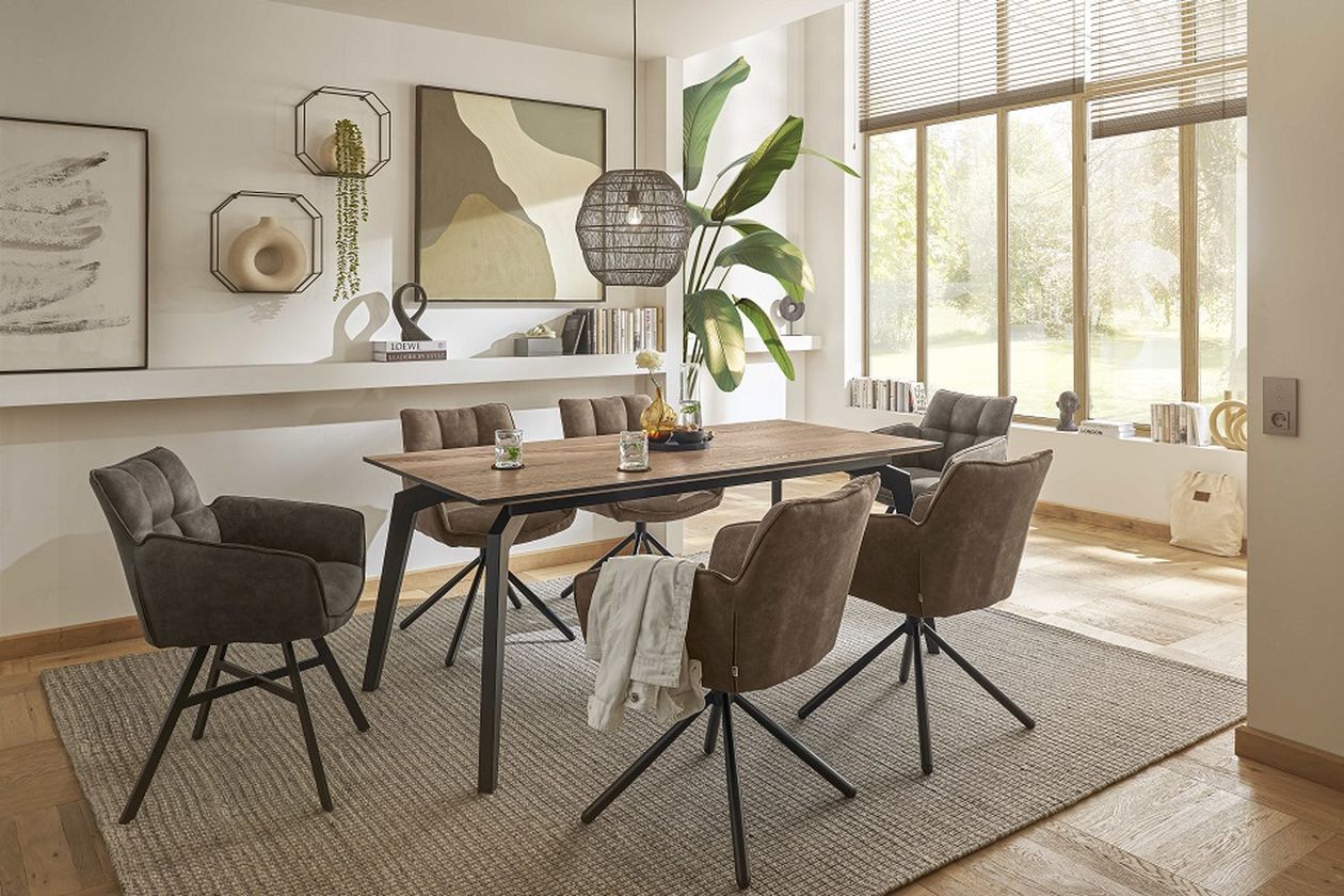 Modernes Esszimmer mit Holztisch, sechs gepolsterten Stühlen, abstrakter Wandkunst, großer Pflanze und Pendelleuchte in der Nähe eines großen Fensters.