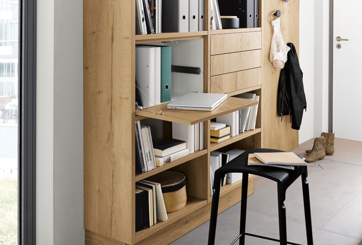 Eingebaute Eichenregale mit ausklappbarem Schreibtisch für Laptop, Bücher und Ordner; schwarzer Hocker, Mantel und Stiefel neben einer weißen Tür.
