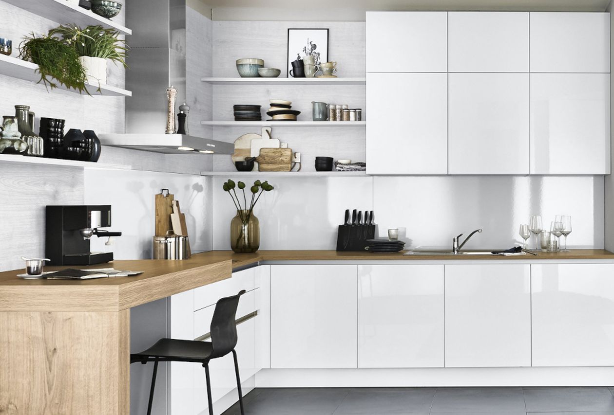 Helle, moderne Küche mit glänzend weißen Schränken, L-förmiger Theke aus Holz mit Barhocker, offenen Regalen, Dunstabzugshaube aus Edelstahl und grauem Fliesenboden.