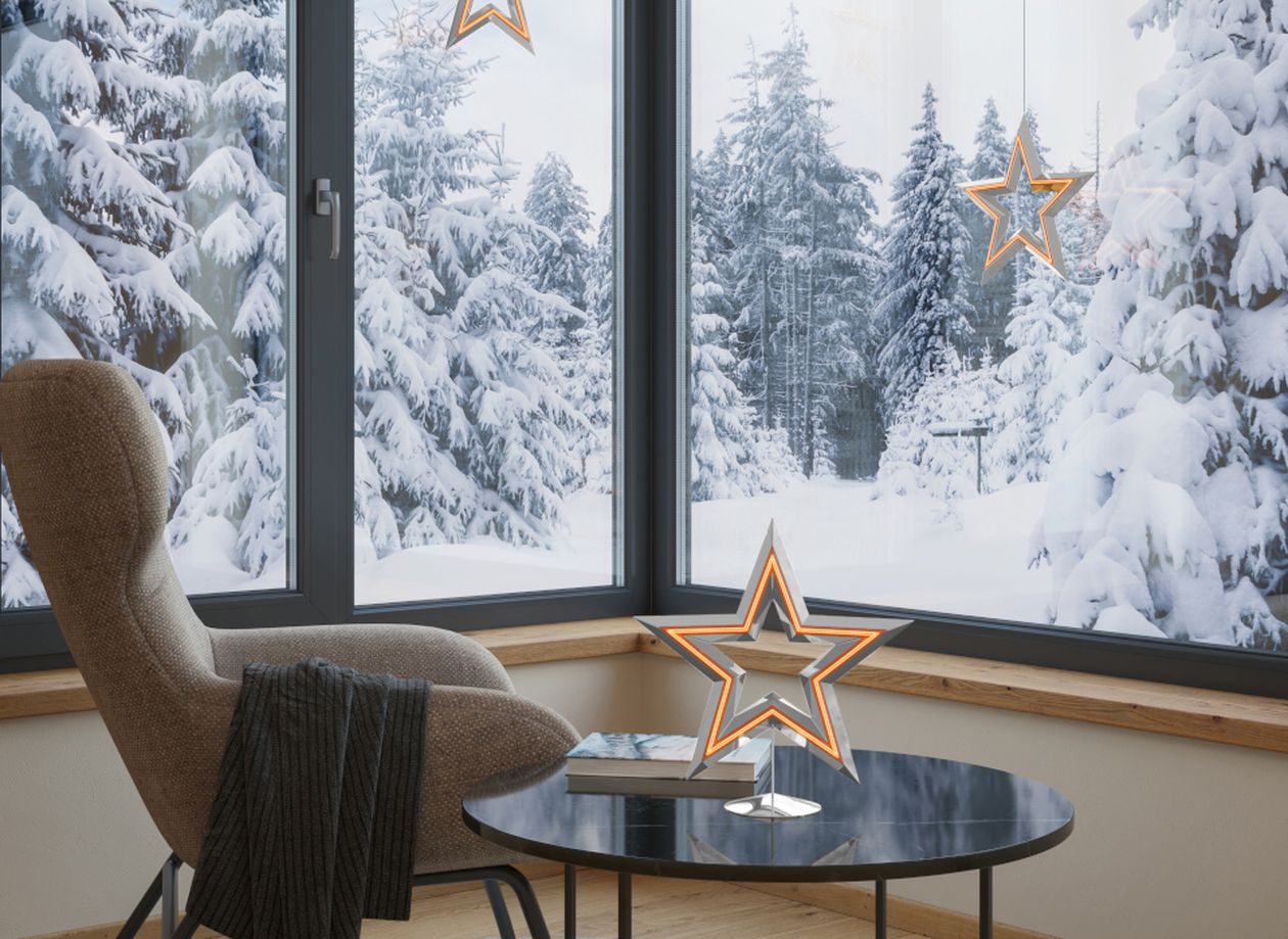 Gemütliche Leseecke mit Sessel, Beistelltisch und leuchtendem Stern-Dekoelement vor einem großen Fenster mit winterlicher Schneelandschaft.