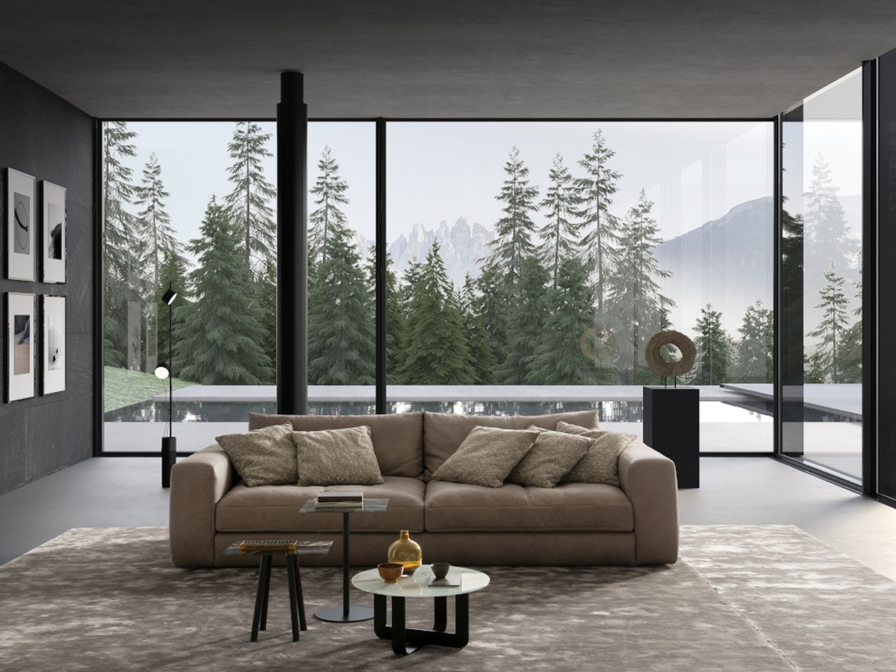 Großzügiges Wohnzimmer mit beigem Sofa, großen Schiebefenstern und Blick auf einen Wald sowie einen Pool im Hintergrund. Eine Skulptur und ein runder Beistelltisch ergänzen die Einrichtung.