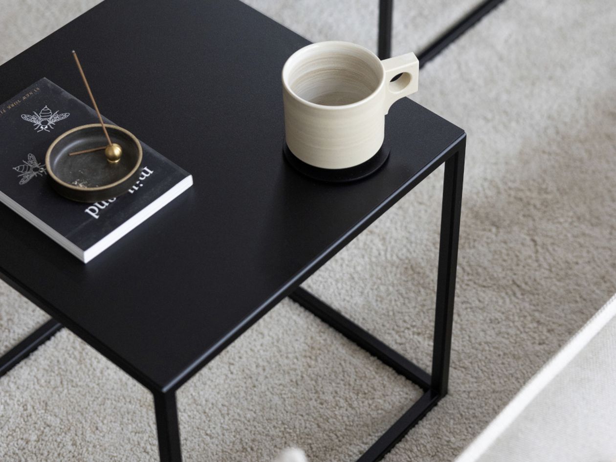 Schwarzer Beistelltisch mit einer Tasse, einem Buch und einem Räucherstäbchenhalter.