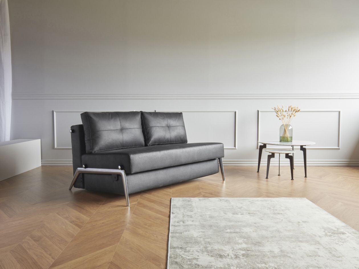 Dunkles Sofa mit zwei Kissen in einem hellen Raum mit weißer Wandverkleidung und einem runden Beistelltisch.