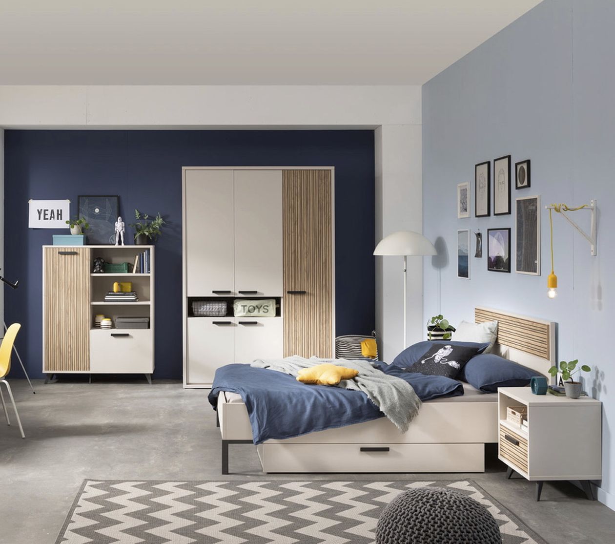Modernes Schlafzimmer mit hellblauen Wänden, Holzmöbeln, einem Bett mit blauer Bettwäsche und einem gemusterten Teppich. Zur Dekoration gehören Wandbilder und eine Stehlampe.