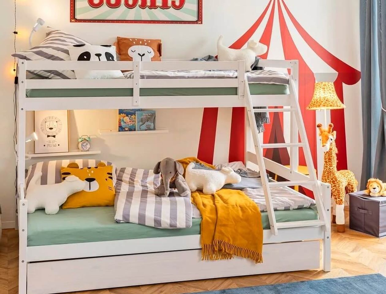 Weißes Kinderetagenbett im Circus-Stil mit buntem Zirkuszelt-Wandbild im Hintergrund, dekoriert mit Tier-Kuscheltieren und gestreifter Bettwäsche.