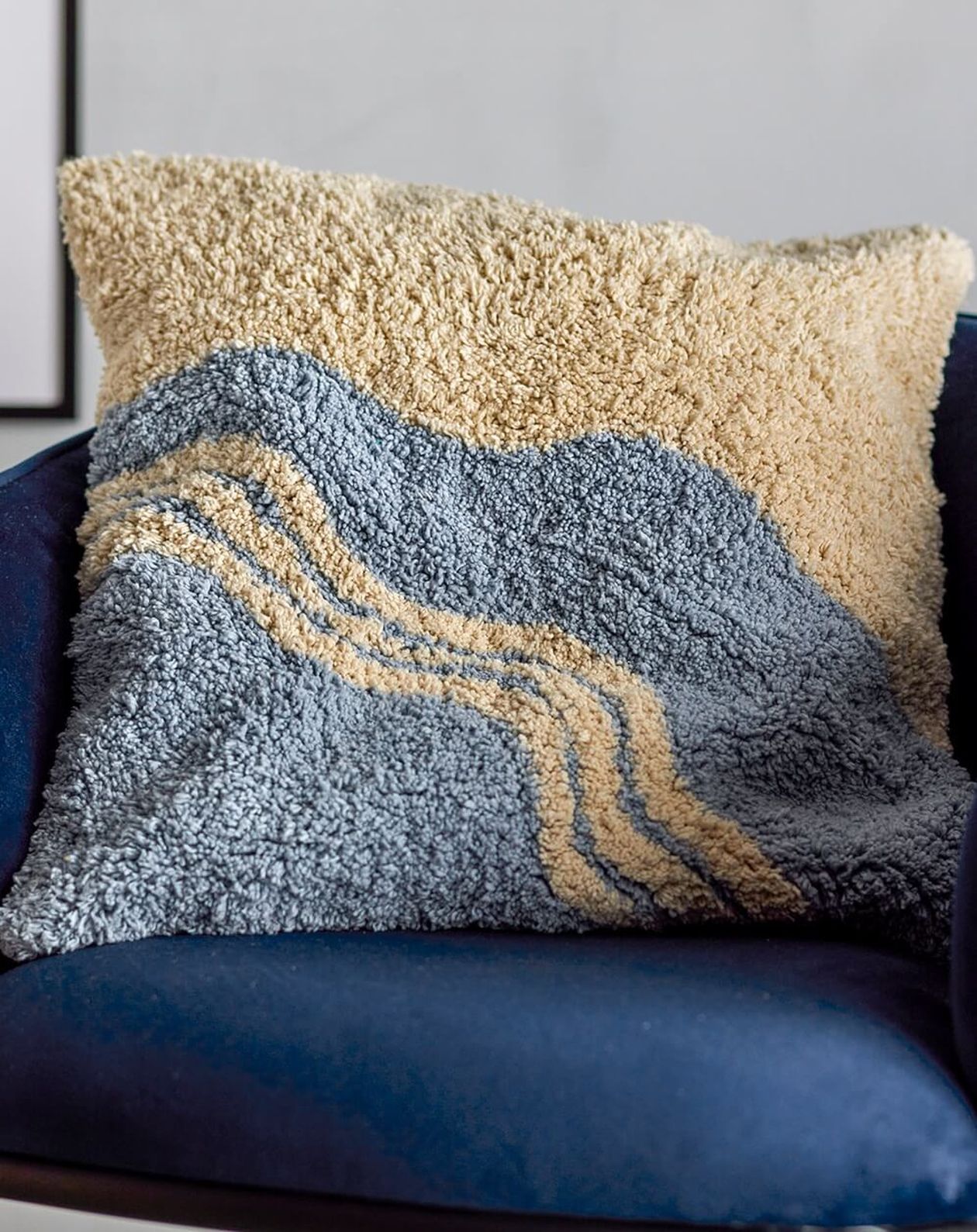 Gemustertes Zierkissen in Hellblau und Beige mit wogendem Linienmuster auf einem dunkelblauen Sessel.