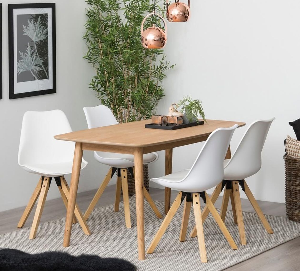 Esstisch aus hellem Eichenholz mit vier weißen Schalenstühlen auf Holzbeinen, darüber kupferfarbene Kugelpendelleuchten und eine Bambuspflanze im Hintergrund.