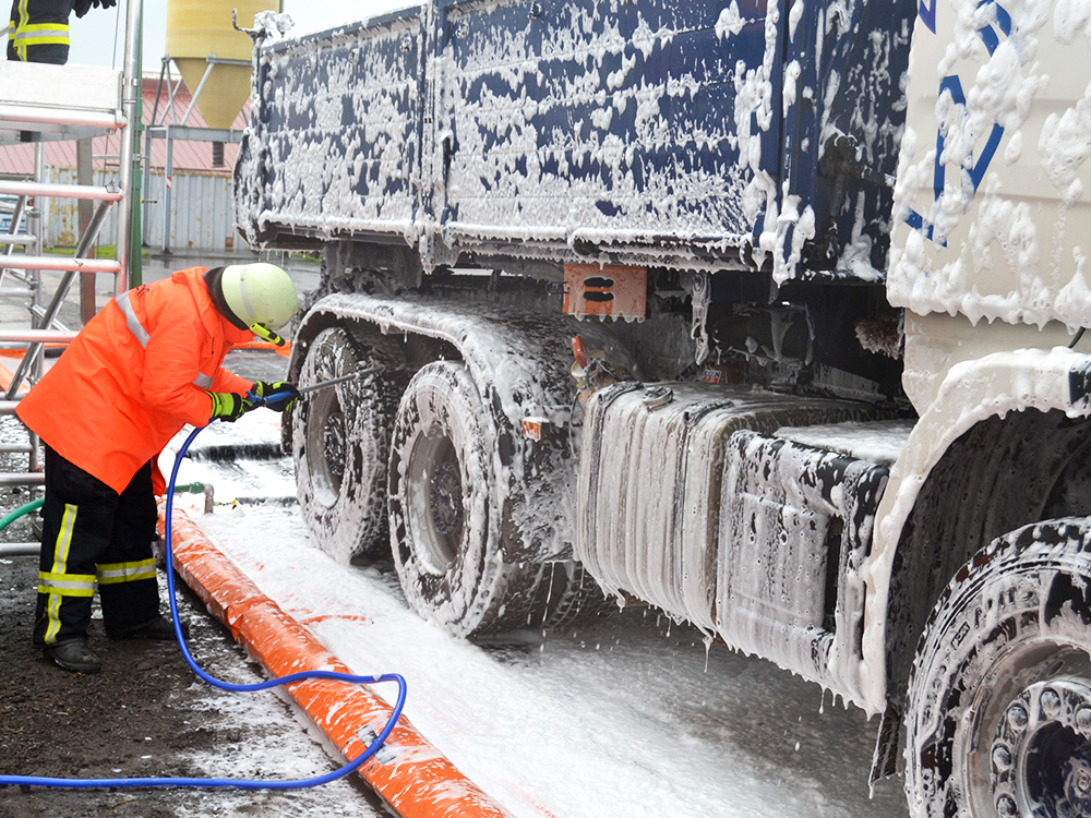 Person in Schutzkleidung dekontaminiert einen LKW mit einem Schaumsprühgerät