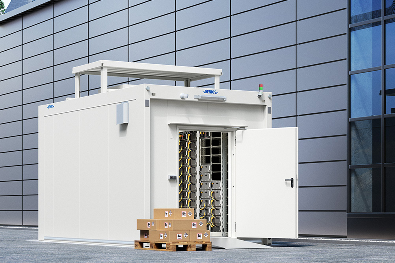 Egy nyitott ajtóval rendelkező fehér ipari konténer áll egy modern, fényvisszaverő üveggel és fém panelekkel ellátott épület előtt. A közelben kartondobozok hevernek egymásra rakva.