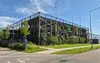 Moderne parkeergarage met een groene gevel, voorzien van een verticale tuin en een gaasstructuur, onder een helderblauwe lucht.