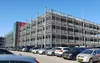 Een parkeergarage met meerdere verdiepingen, aangeduid als "P3", met enkele geparkeerde auto's op de voorgrond onder een helderblauwe lucht.