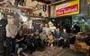 Een groep mensen poseert samen in een warm verlichte ruimte met een vintage-uitstraling, diverse decoratieve elementen en een bord met de tekst "Vins Gaillard" op de achtergrond.