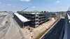 Bouwplaats van een parkeergarage met meerdere verdiepingen nabij wegen, met kranen en bouwmaterieel op een zonnige dag.