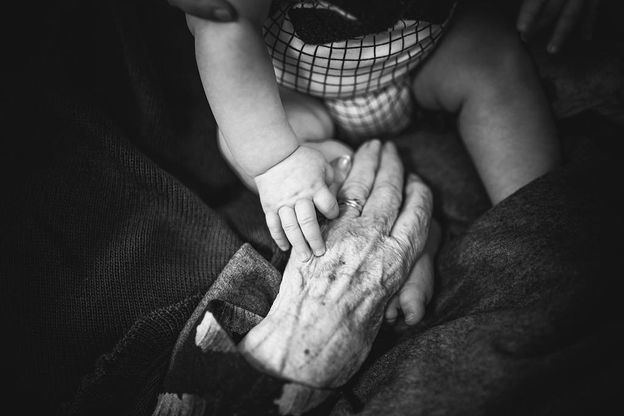 Eine Babyhand hält die Hand einer alten Frau