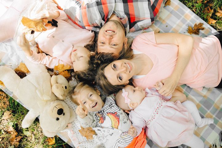 Familie liegt lachend mit Kindern und Teddybär auf einer Picknickdecke im Herbstlaub