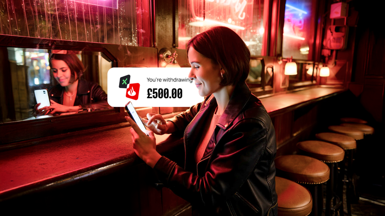 A woman in a leather jacket uses her phone at a bar, withdrawing £500.00, with a bright neon-lit mirror and empty barstools in the background.