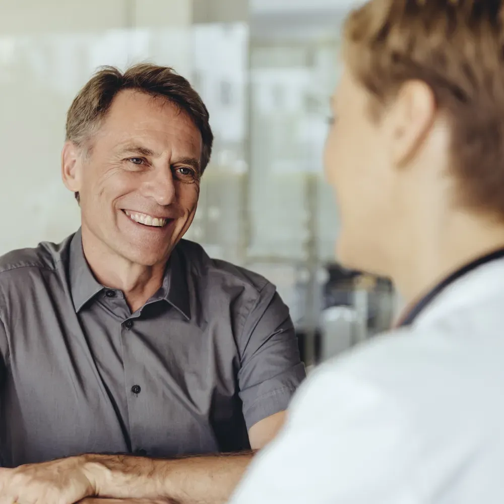 Two people having a conversation at a table, one smiling and wearing a gray shirt, the other with short hair, seen from the back.