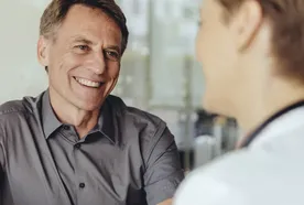 Two people having a conversation at a table, one smiling and wearing a gray shirt, the other with short hair, seen from the back.