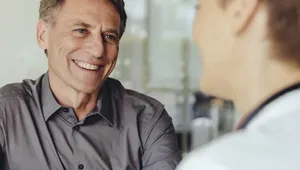 Two people having a conversation at a table, one smiling and wearing a gray shirt, the other with short hair, seen from the back.