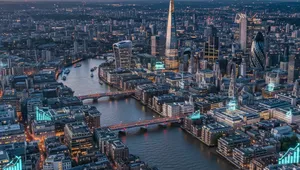 Aerial view of London's skyline at dusk, featuring the Thames River, illuminated buildings, and iconic skyscrapers like The Shard.