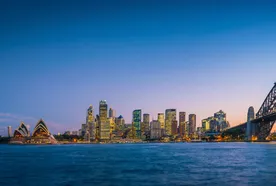 Skyline of Sydney at dusk, featuring the Opera House, lit skyscrapers, and the Harbour Bridge over calm water.