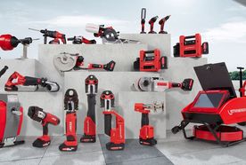 Various red and black construction tools displayed on tiered concrete platforms, including drills, saws, and pipe cutters, against a white wall.