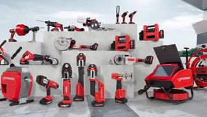 Various red and black construction tools displayed on tiered concrete platforms, including drills, saws, and pipe cutters, against a white wall.