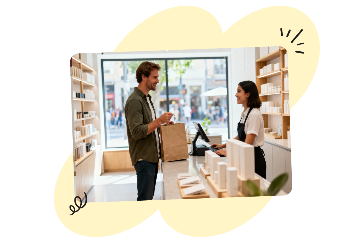 Man holding a paper bag, smiling at a cashier in a bright store with shelves of products and a large window in the background.