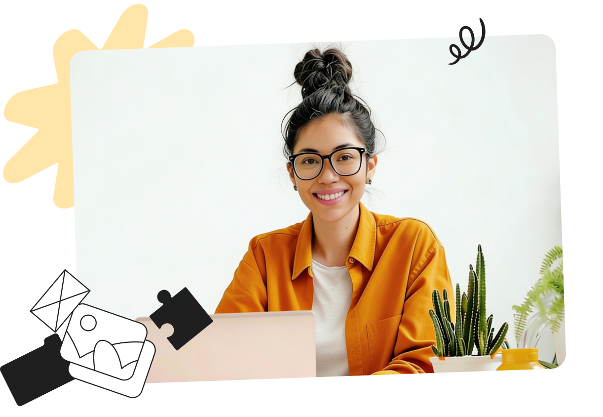 Smiling person with glasses and a top bun, wearing a yellow shirt, sitting at a desk with a laptop and plants in the background.