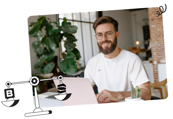 Smiling man with glasses working on a laptop at a table, with indoor plants and modern room decor in the background.